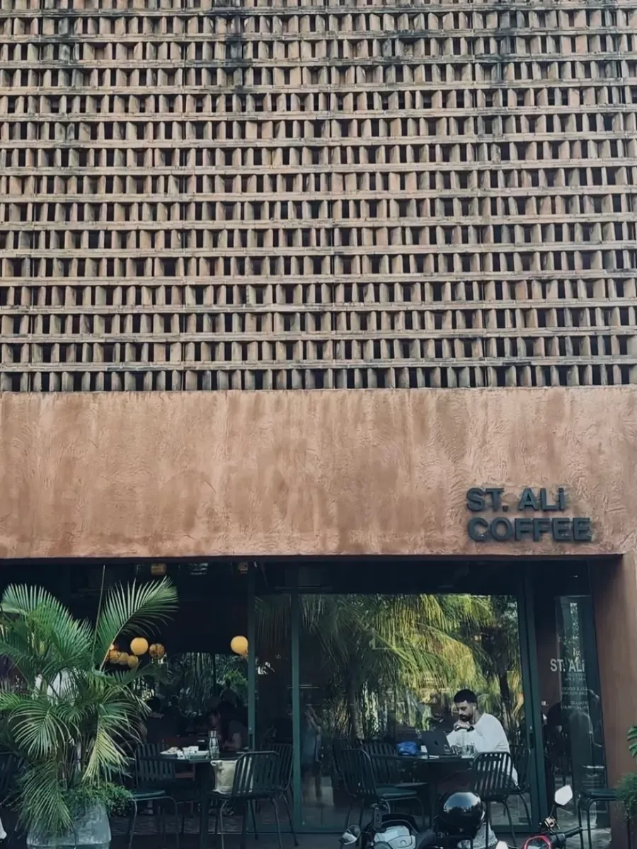 The ST. ALi Coffee facade with brick lattice screening, outdoor tables, and a laptop open at a sidewalk seat