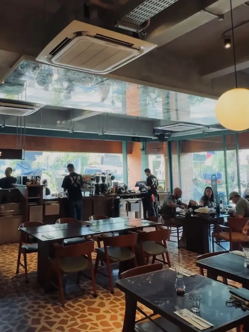Looking across the indoor dining room toward the bar, communal table, and street openings, with a mirrored ceiling panel overhead