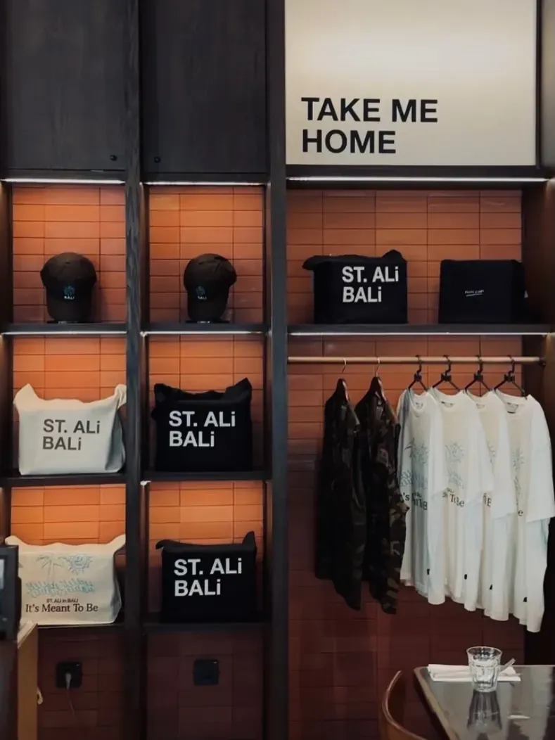 Take Me Home retail wall with ST. ALi Bali tote bags, caps, and It's Meant To Be shirts on terracotta tile