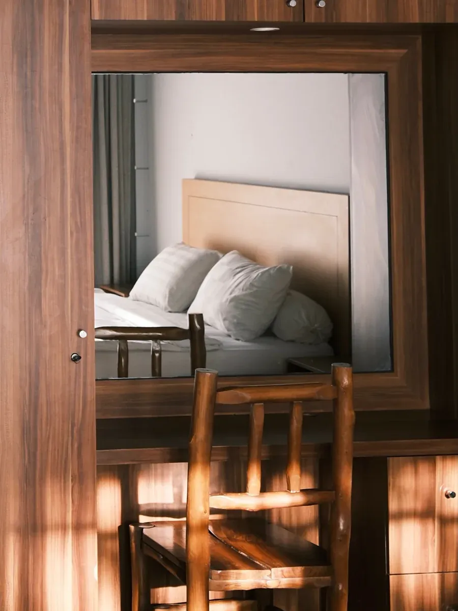 Dark wood vanity and desk with a rustic branch chair, mirror reflecting the bed