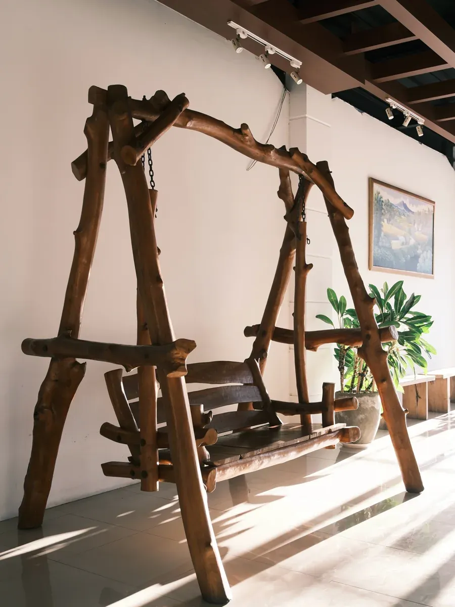 Rustic wooden log swing in a bright common room with a potted plant and framed art