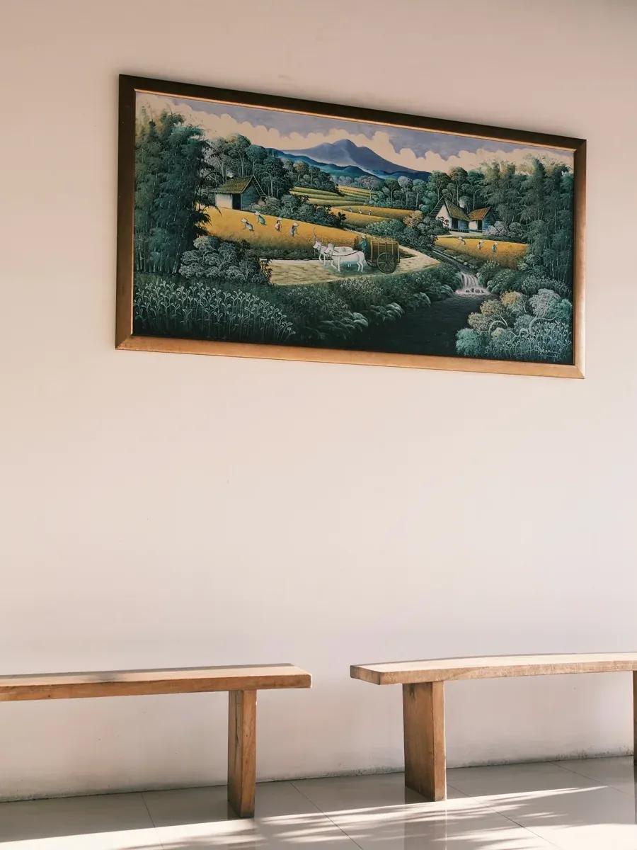 Framed landscape painting above two wooden benches on a light tiled hallway wall