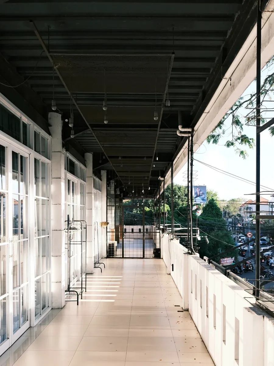 Covered outdoor balcony walkway overlooking the street, with hanging bulbs and glass doors
