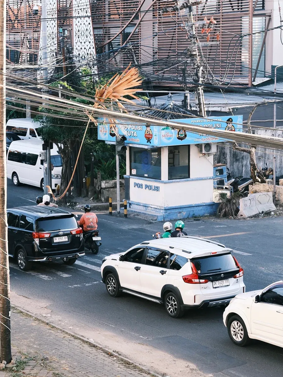 Street intersection below with scooters, cars, tangled wires, and a Pos Polis booth