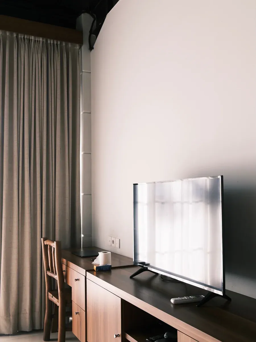 Dark wood console with a television, remote, and wooden chair beside floor-length curtains