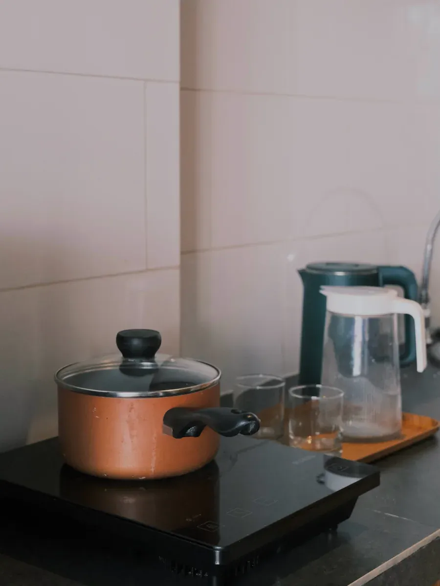 Copper pot on a black induction cooktop beside drinking glasses and a pitcher