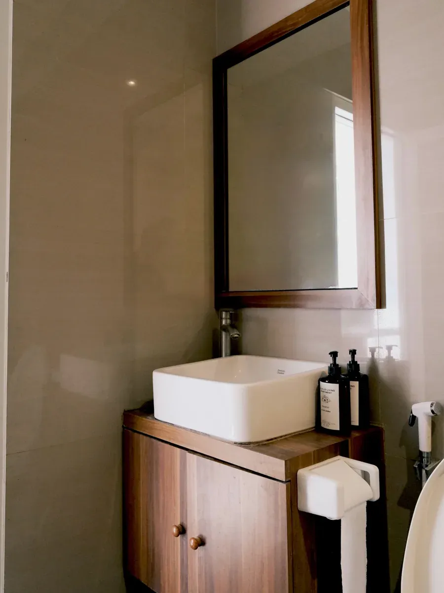 Bathroom vanity with a white vessel sink, wood cabinet, framed mirror, and soap bottles