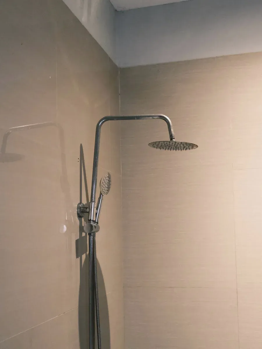 Chrome rain shower and handheld sprayer mounted on beige bathroom tile