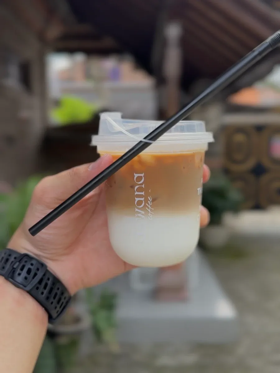 A hand holding an iced coffee in the hostel courtyard