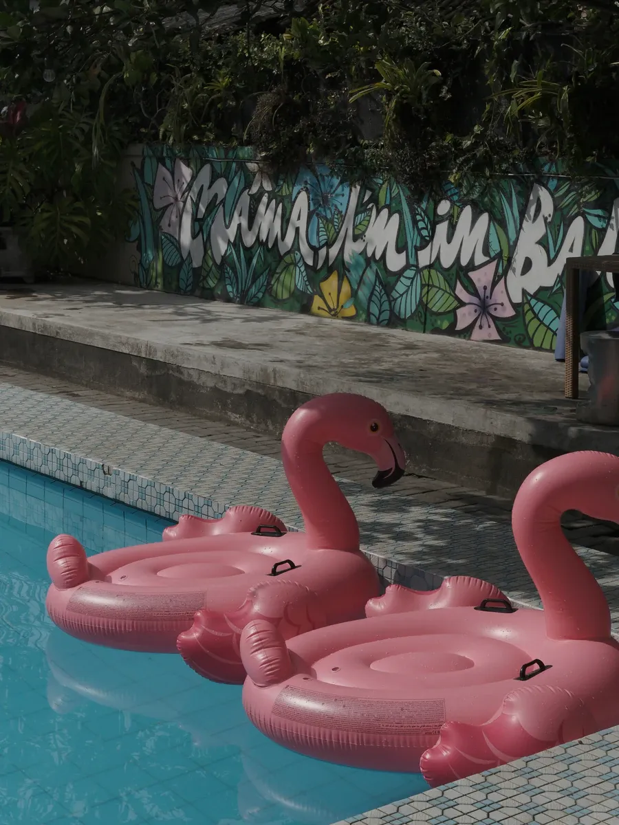 Pink flamingo pool floats in the swimming pool in front of the mural