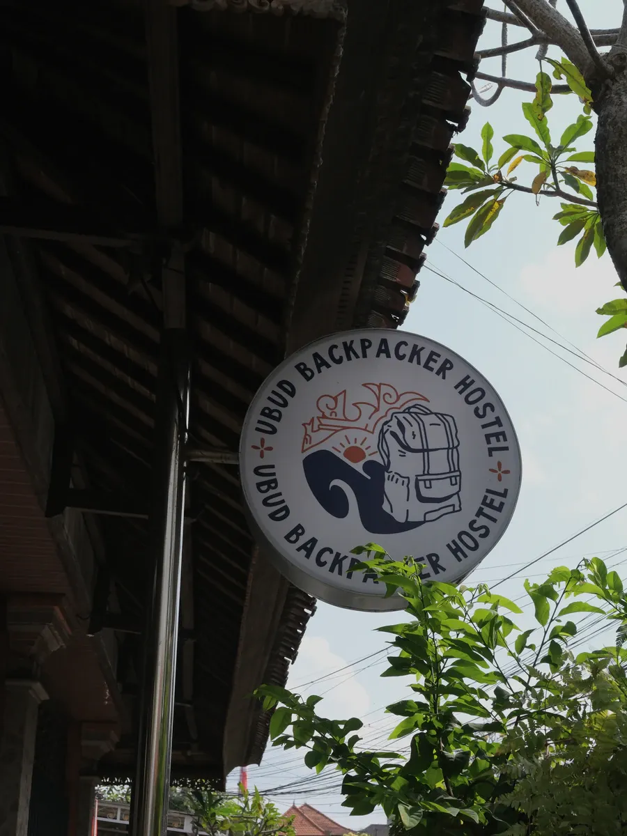 The round Ubud Backpacker Hostel sign hanging from the eaves